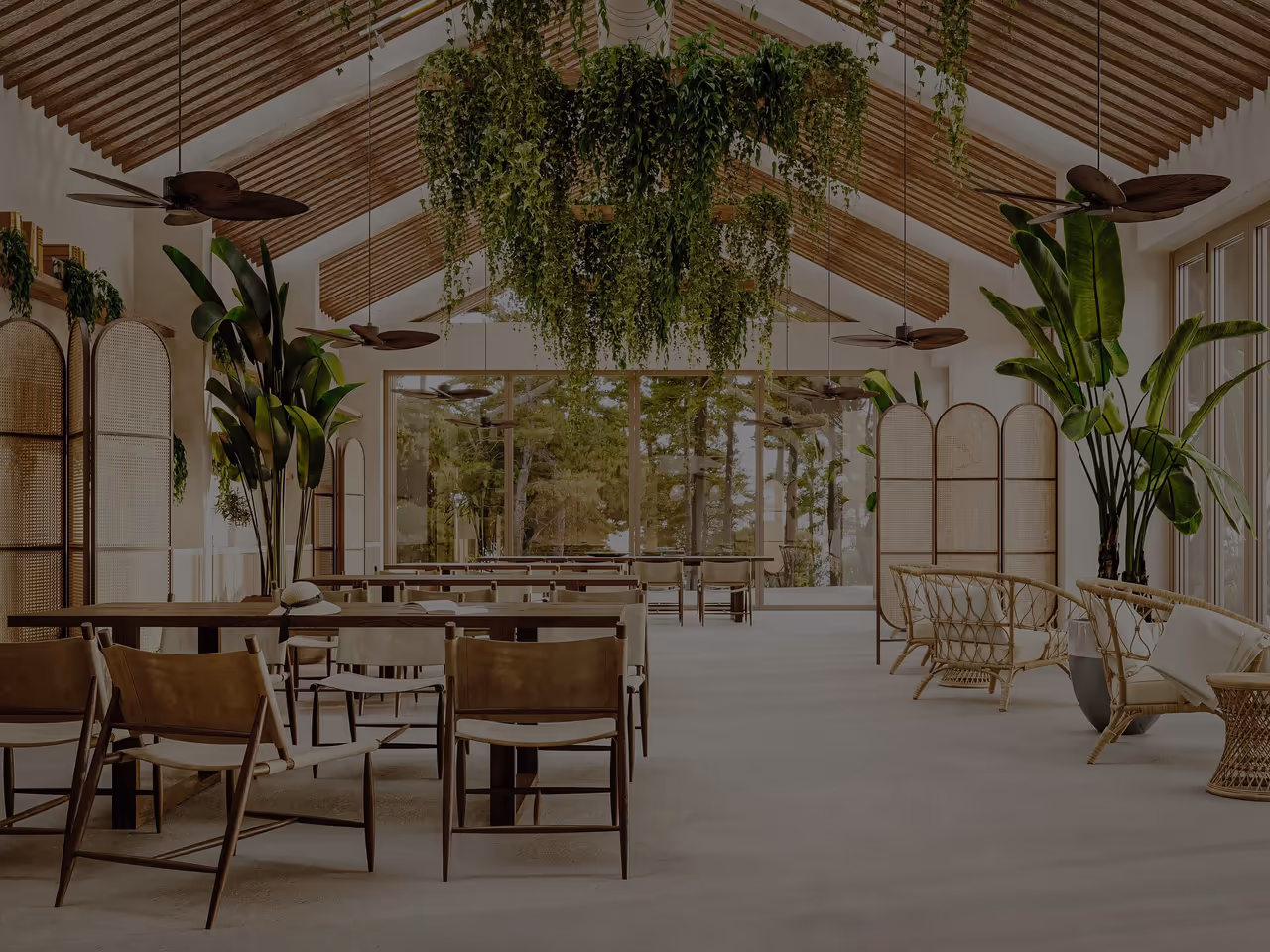 Sala sob um tecto de duas águas em ripado de madeira, com ventoinhas e vegetação suspensa, mesas compridas com cadeiras de couro e poltronas de vime.