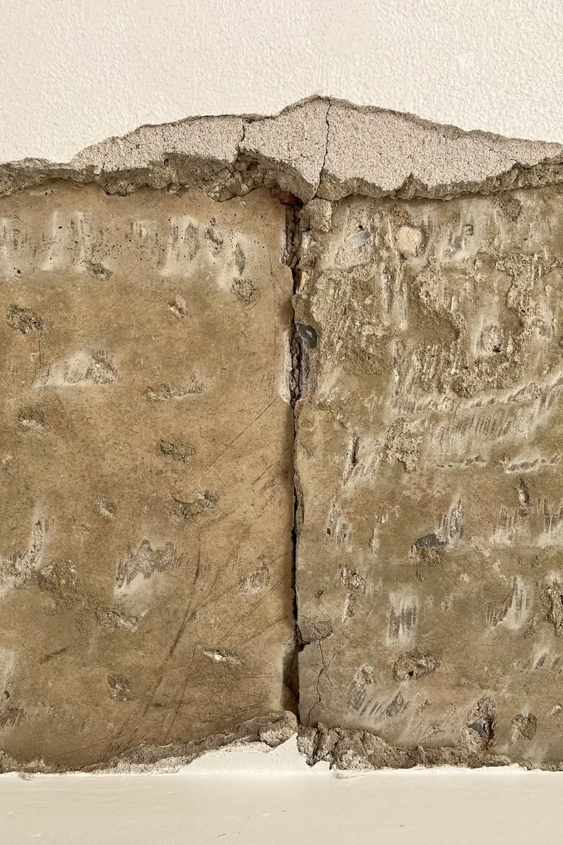 Um detalhe de parede com uma faixa de revestimento retirada, delimitada por revestimento acima e abaixo, e uma linha vertical escura a atravessar a zona exposta.