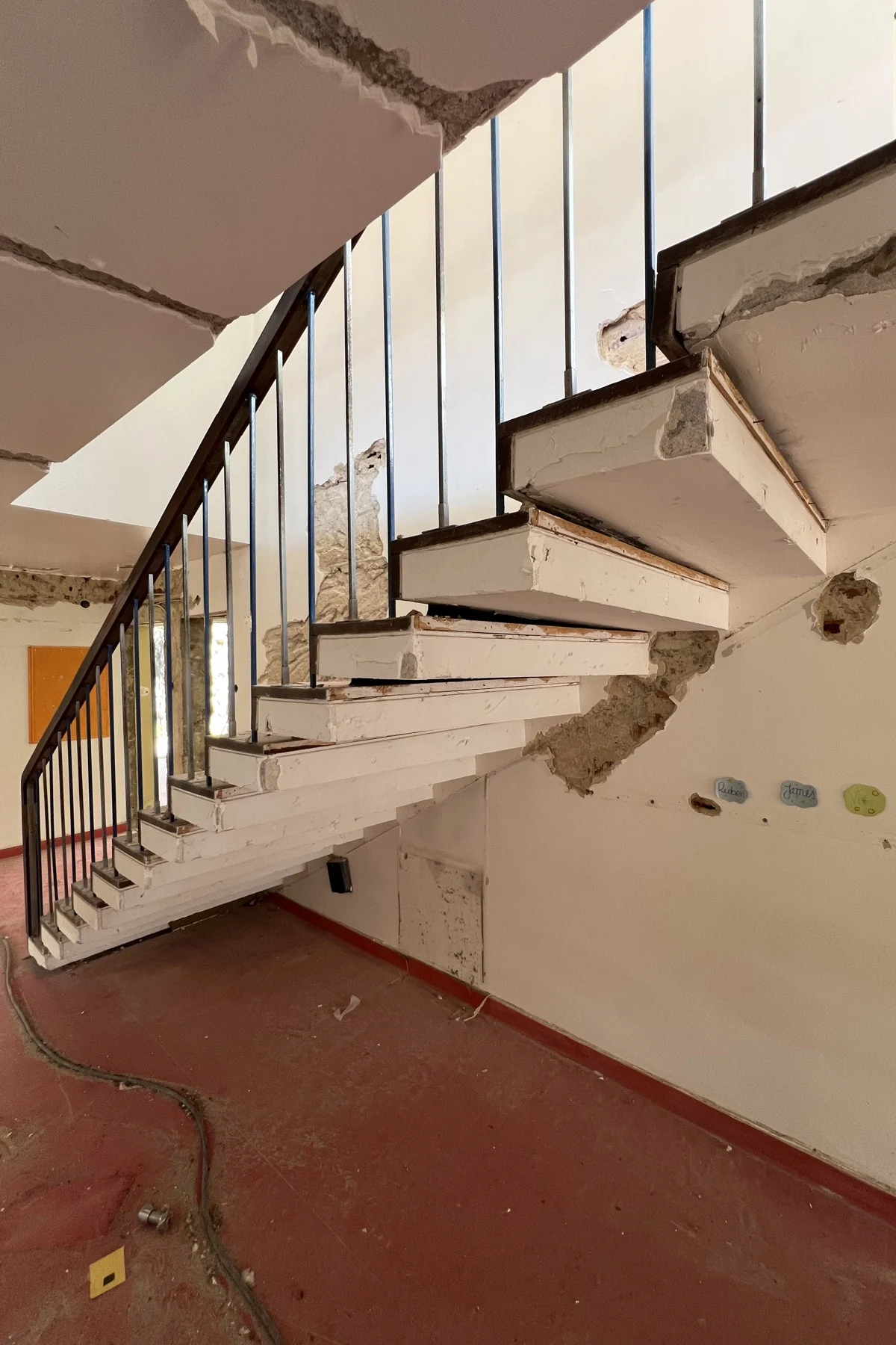 A escada em consola: degraus brancos a sair da parede, sem perna por baixo, guarda de prumos escuros finos, e o revestimento aberto ao longo da parede.