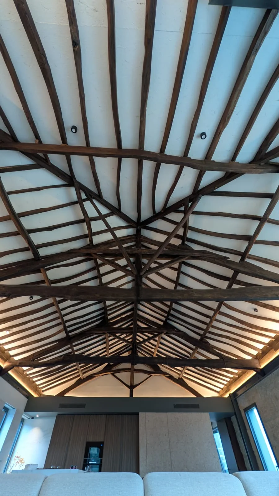 A estrutura de madeira restaurada da cobertura do solar vista directamente de baixo: barrotes escuros a irradiar de um cume central sobre painéis claros, com iluminação de sanca escondida no arranque da parede.