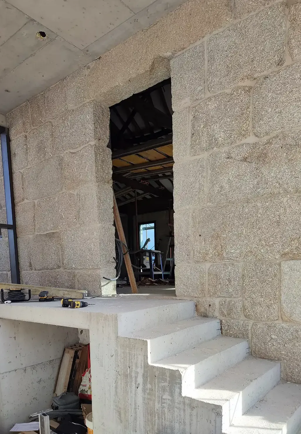 Uma escada de betão branco a subir contra uma parede de blocos grandes de granito.