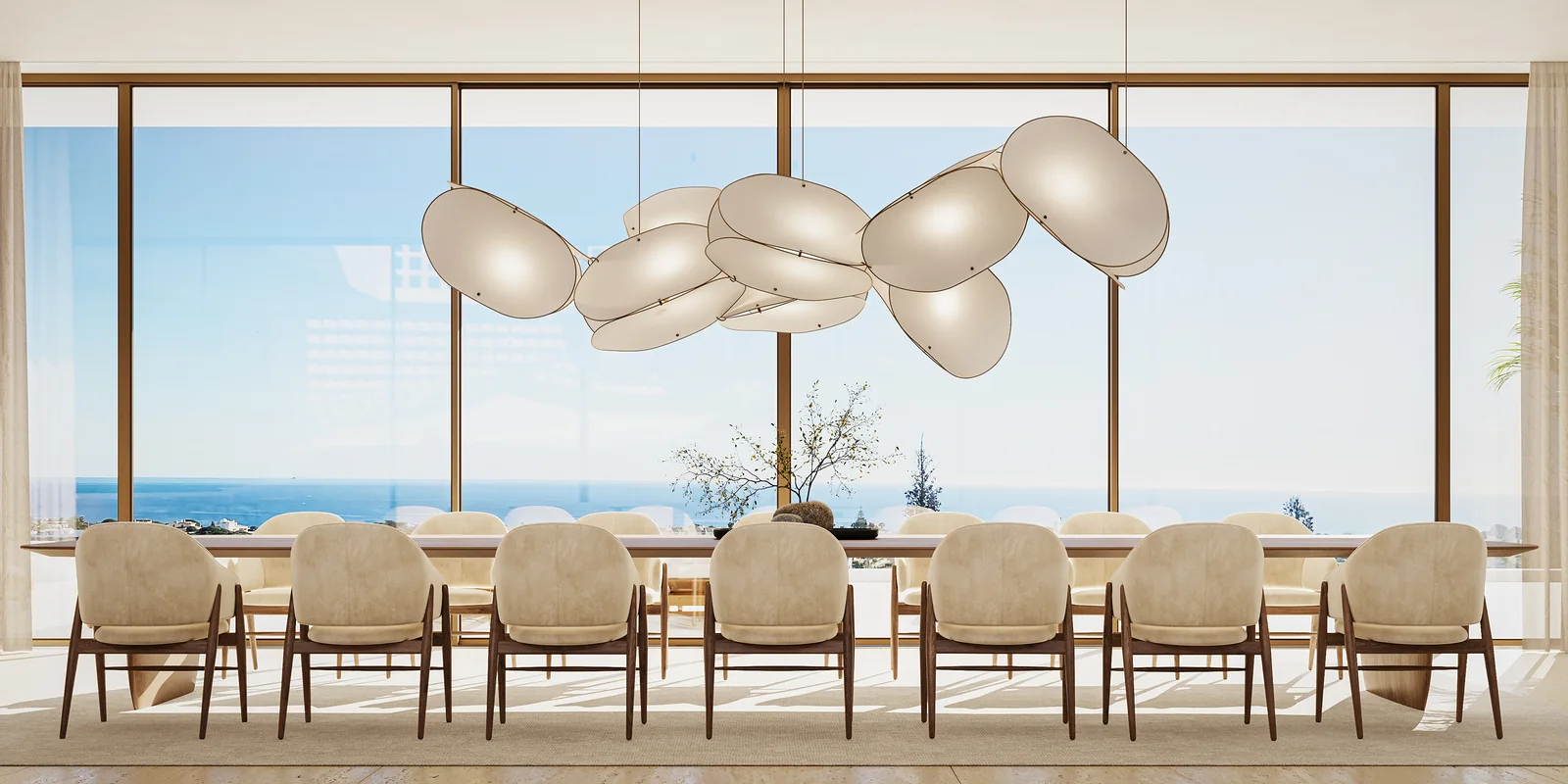A sala de jantar vista de frente: mesa longa para doze contra uma parede de vidro sem interrupção, um conjunto de candeeiros escultóricos claros por cima e o oceano a preencher todo o vão.
