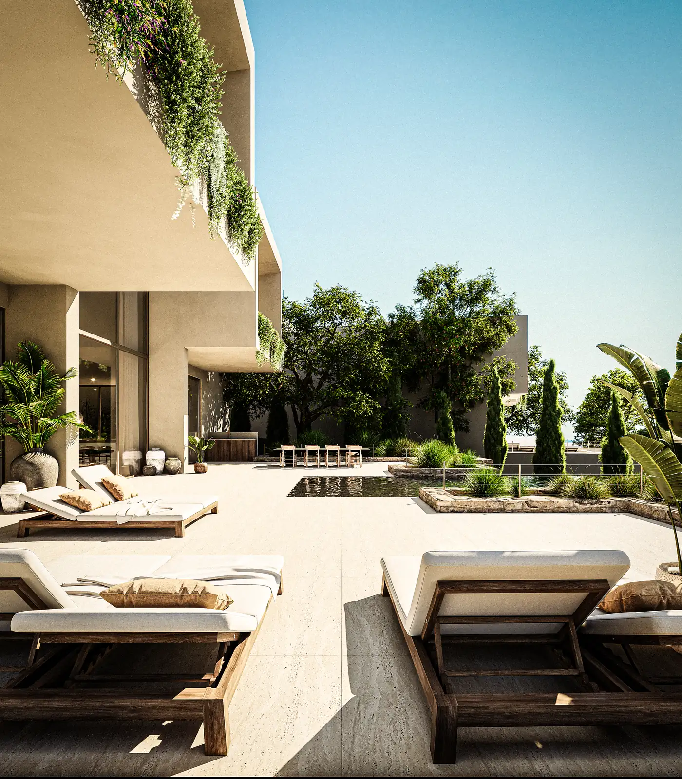 O terraço da piscina ao longo do flanco da casa, espreguiçadeiras em fila sobre pavimento claro, ciprestes e oliveira contra o reboco, e o piso superior em consola a fazer sombra.