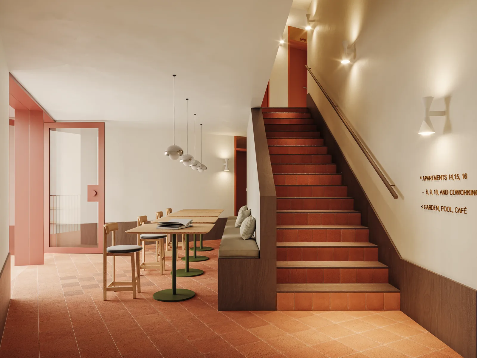 O espaço de trabalho partilhado ao pé da escada principal: degraus em terracota com focinho em madeira, lambril de madeira escura a acompanhar o lanço, letras de sinalética na parede e uma mesa de trabalho com bancos por baixo.